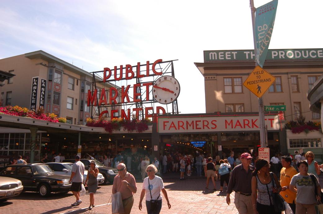 An image of many pedestrians at walking at Pike Place under the Public Market Center sign