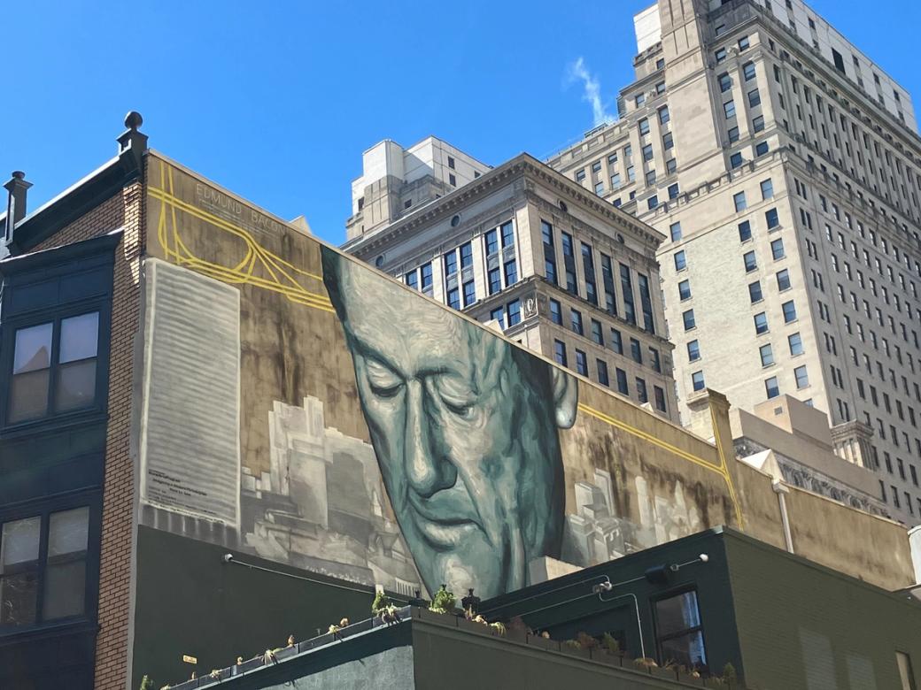 Mural of Edmund Bacon on side of a building. Large buildings stand tall behind it.