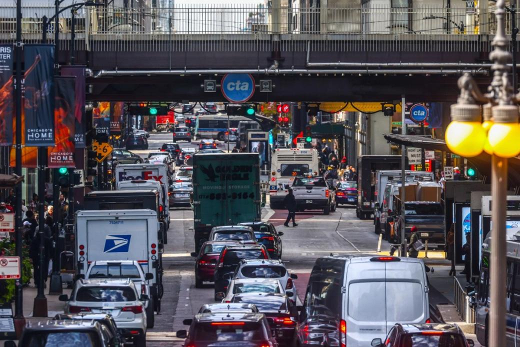 A busy street with a long line of cars. There is a train line overhead as well