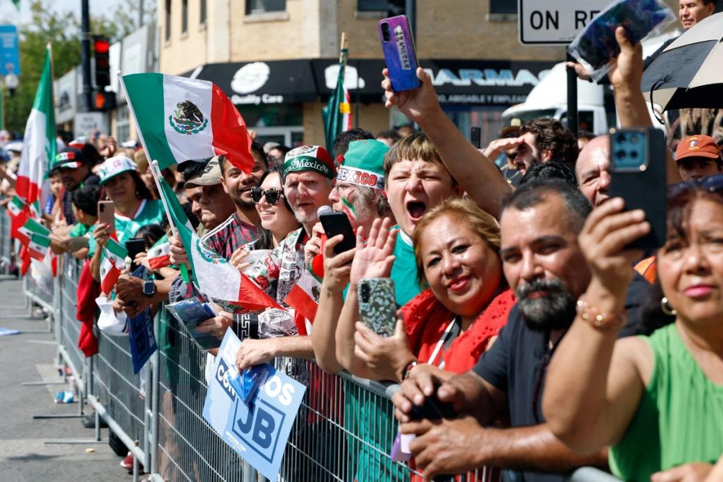 A group of people lined up behind a barrier, cheering and holding up the mexican flag