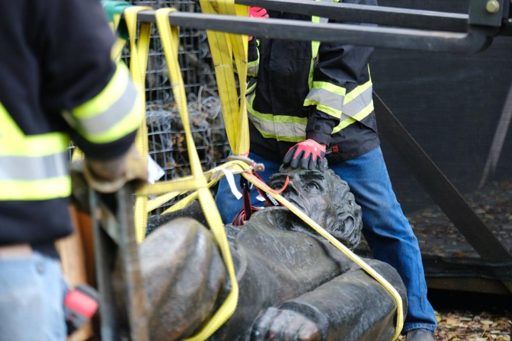 Two people in safety gear hold statue of Lincoln with straps wrapped around it