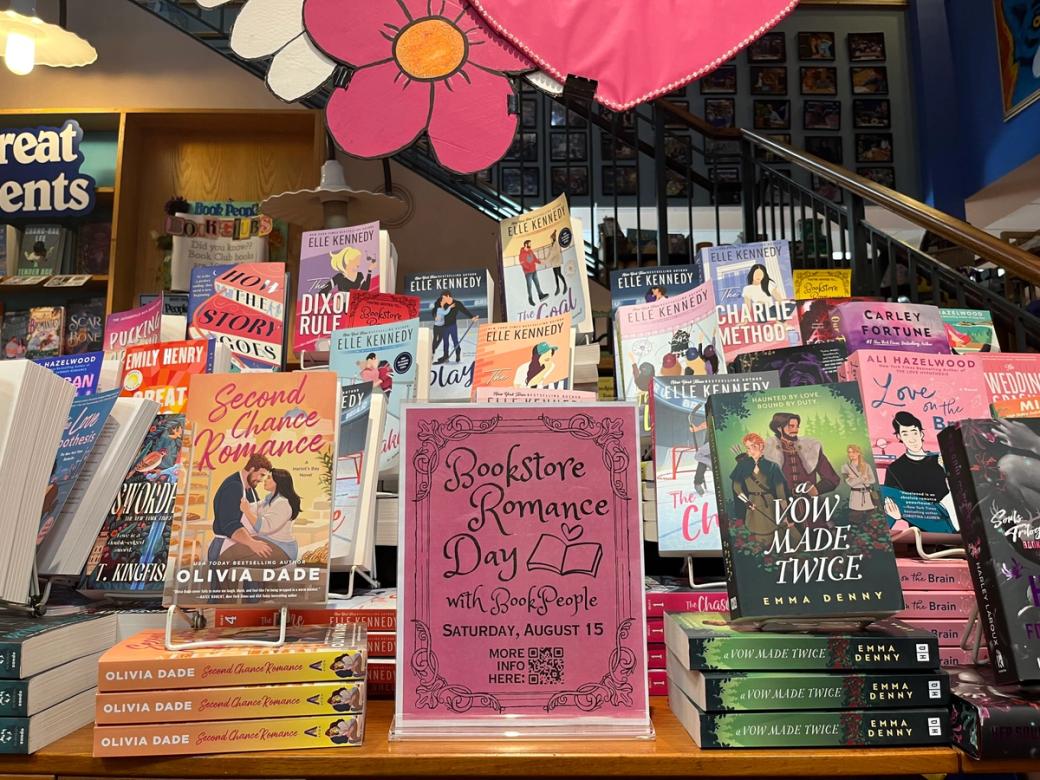 A pink sign that says "Bookstore Romance Day" surrounded by stacks of books.
