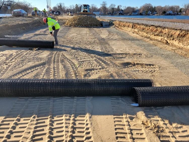 A construction worker moving large black pipes on dirt.