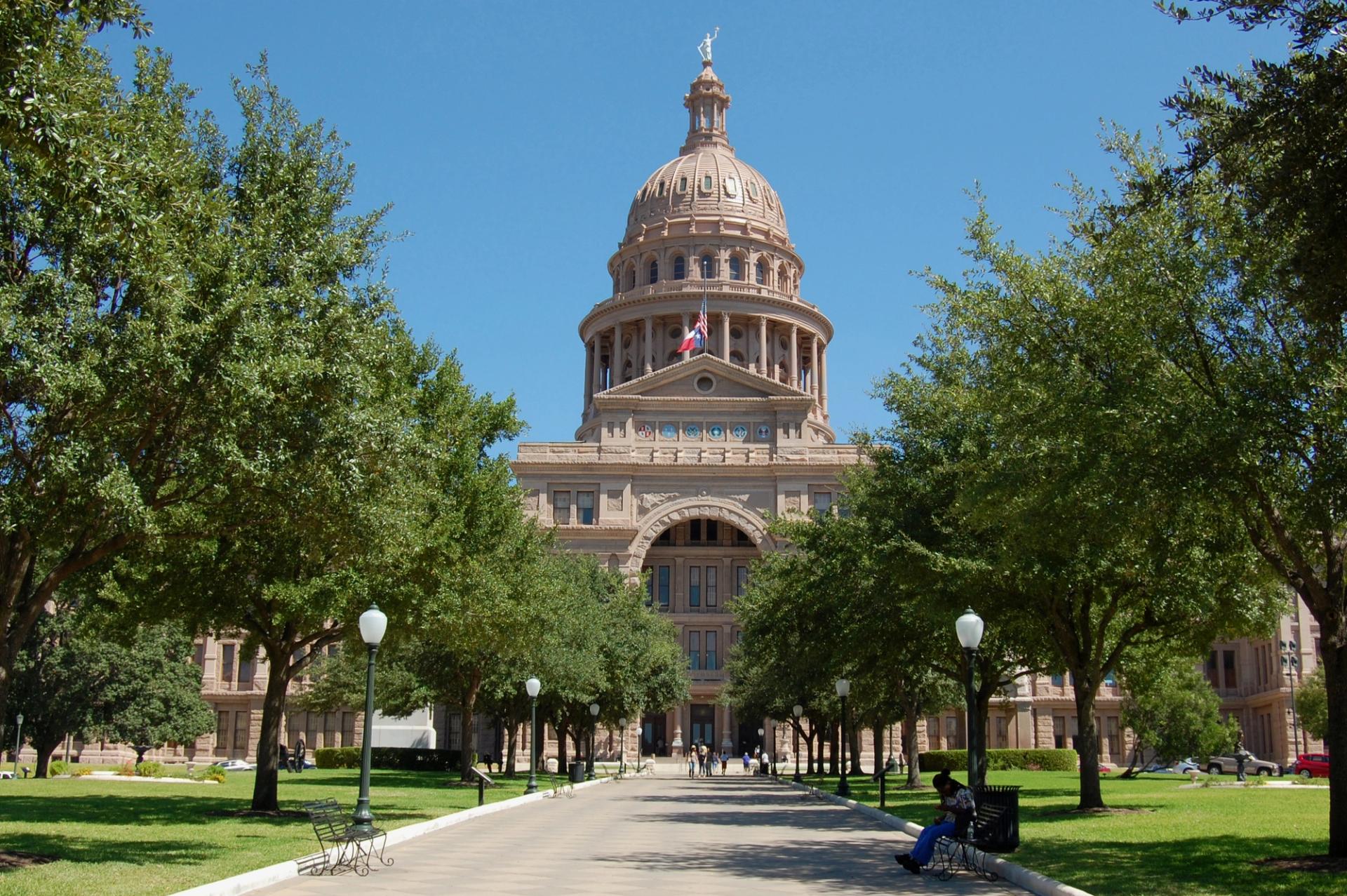 The outside of the Texas Capitol building. The building is lined with trees.