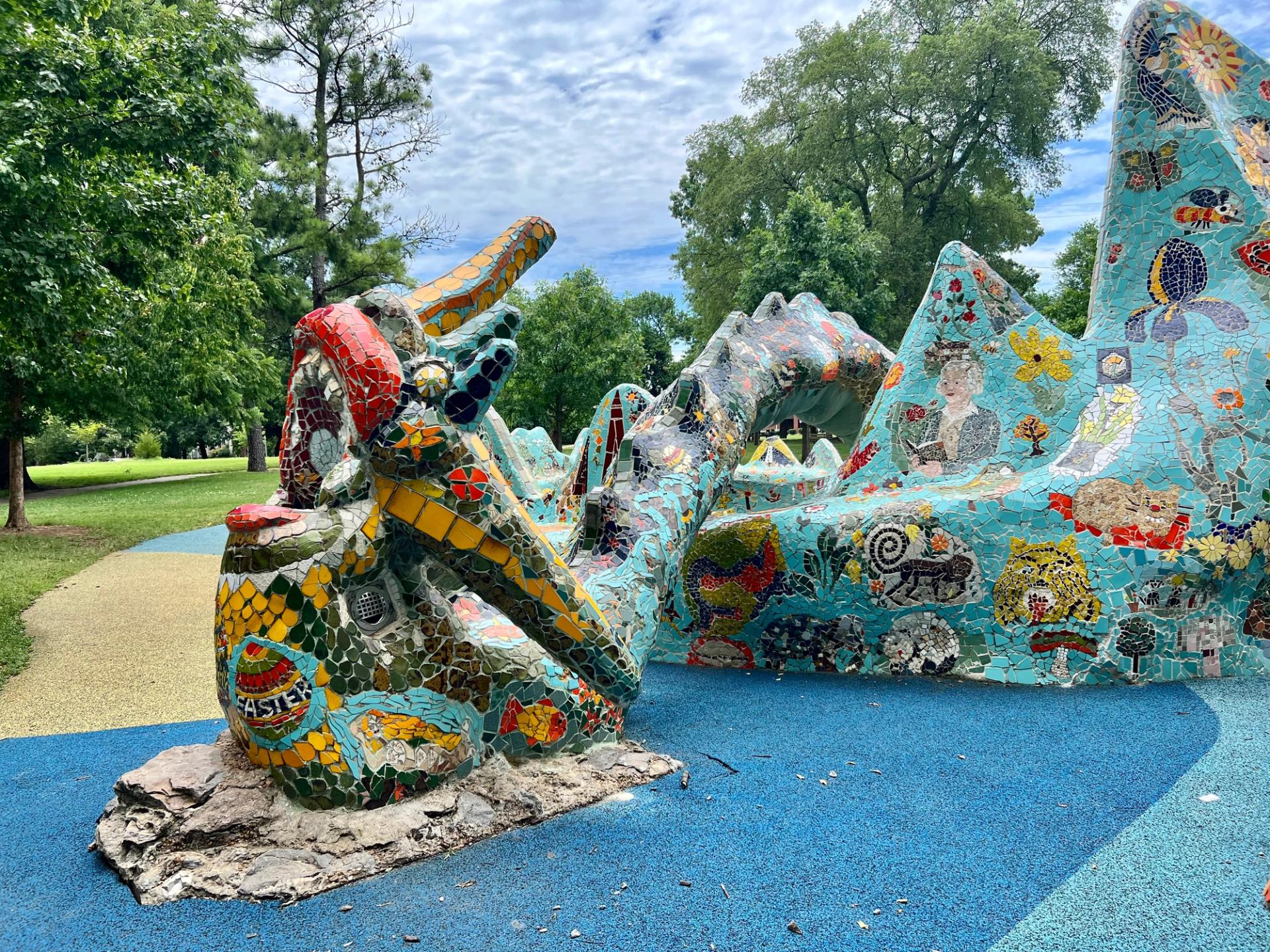 A large teal mosaic dragon sculpture surrounded by trees.
