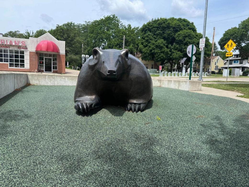 A large bronze bear sits in a square near a building with a red awning.