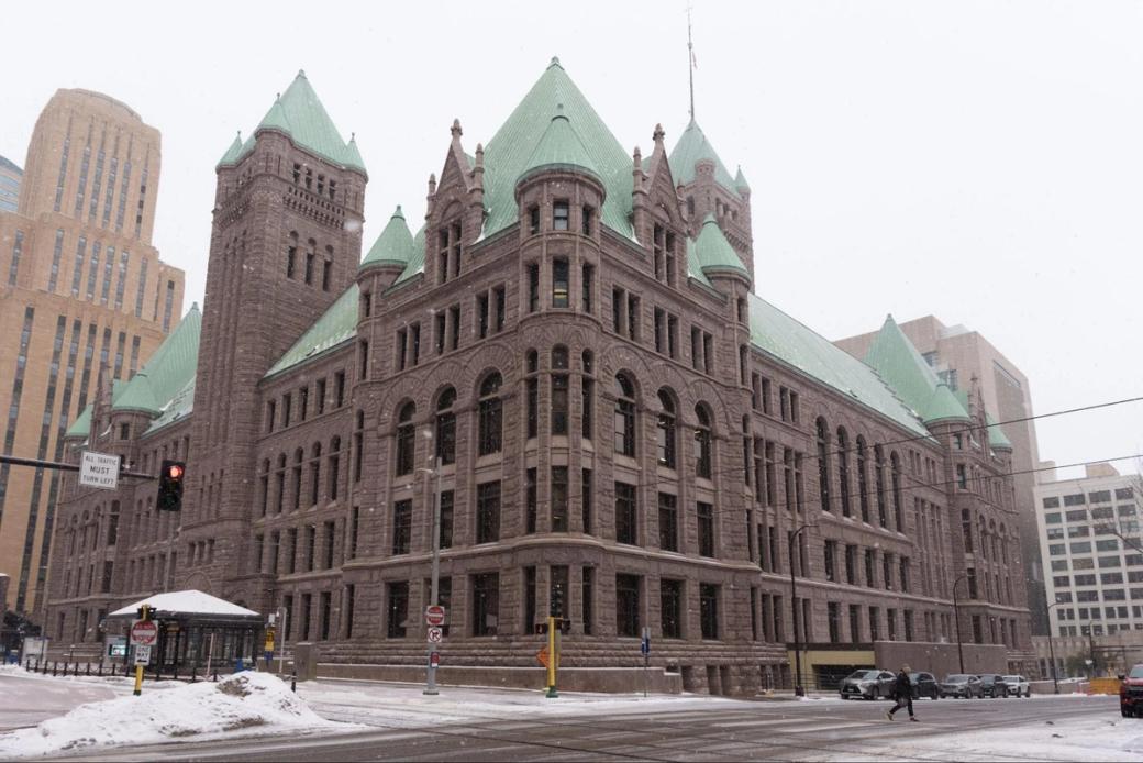Minneapolis City Hall and Hennepin County Courthouse, with its Romanesque architecture and green roof. The intersection can also be seen, with some snow, cars, and pedestrians visible.