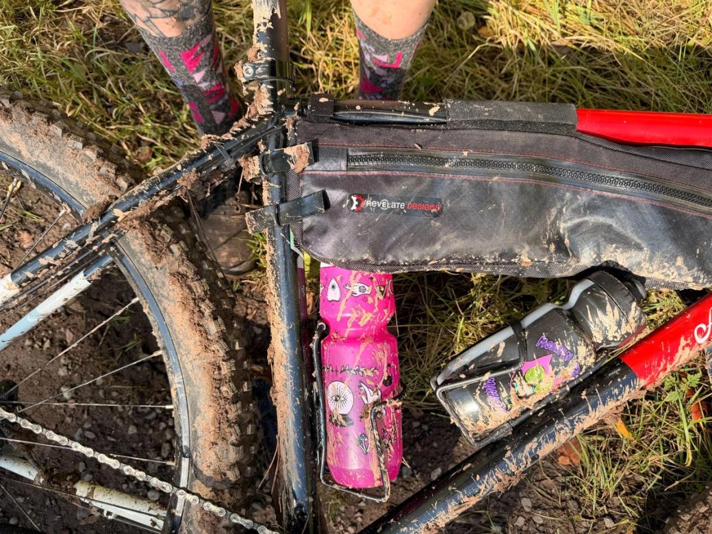A close up of a very muddy mountain bike with a very muddy pink water bottle and a very muddy pair of legs.