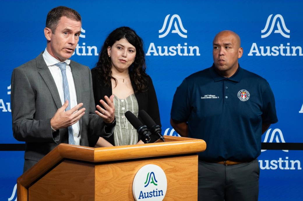District 7 council member Mike Siegel speaks at a podium during a press conference. Austin City Council members Vanessa Fuentes, center, and José Velásquez, right, listen.