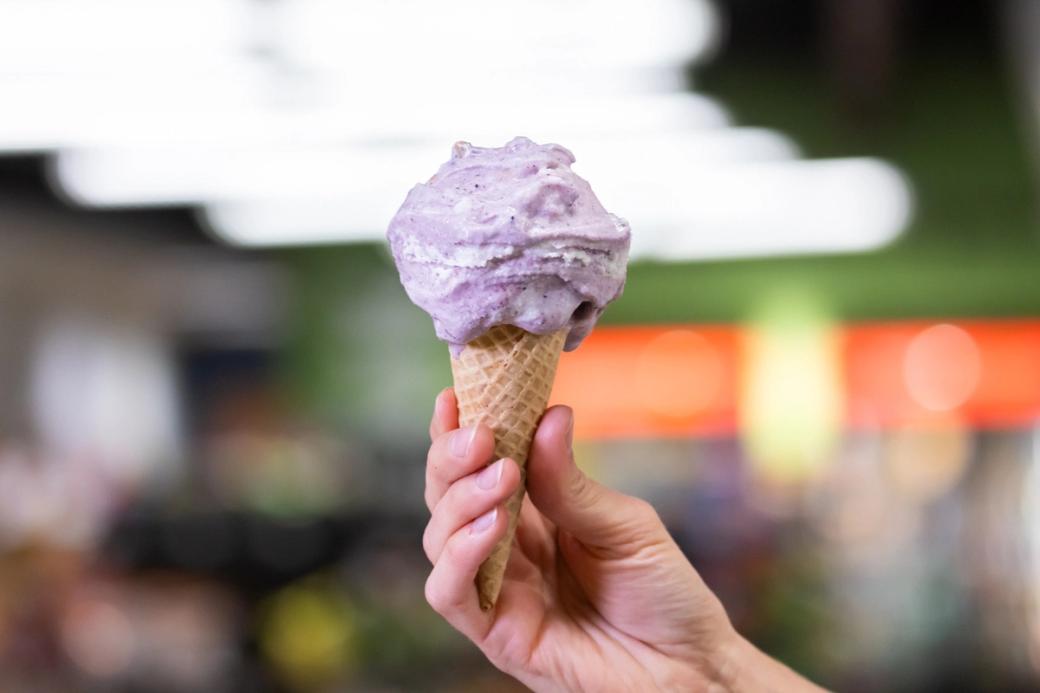 A hand holds a cone of light purple ice cream.