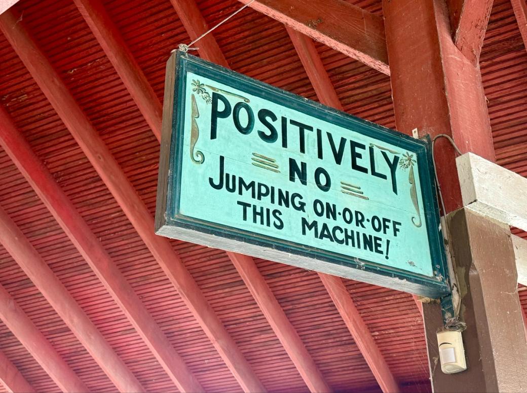A hand-painted wooden sign that says in all-caps: “POSITIVELY NO JUMPING ON OR OFF THIS 