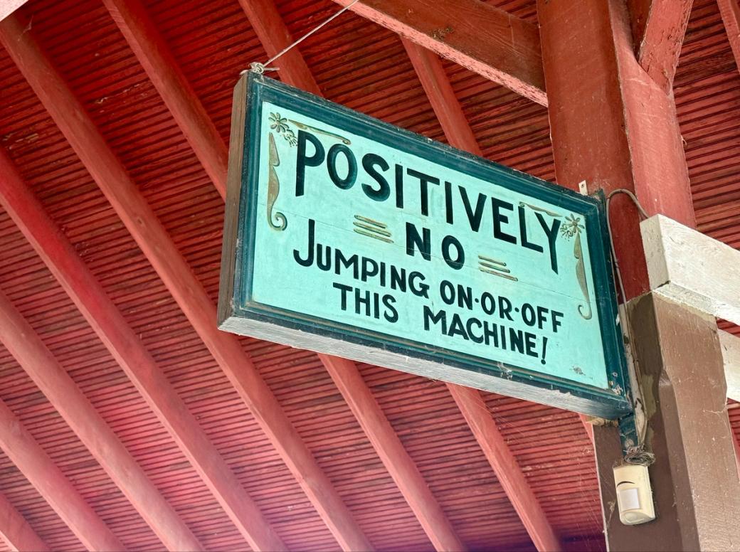 A hand-painted wooden sign that says in all-caps: “POSITIVELY NO JUMPING ON OR OFF THIS