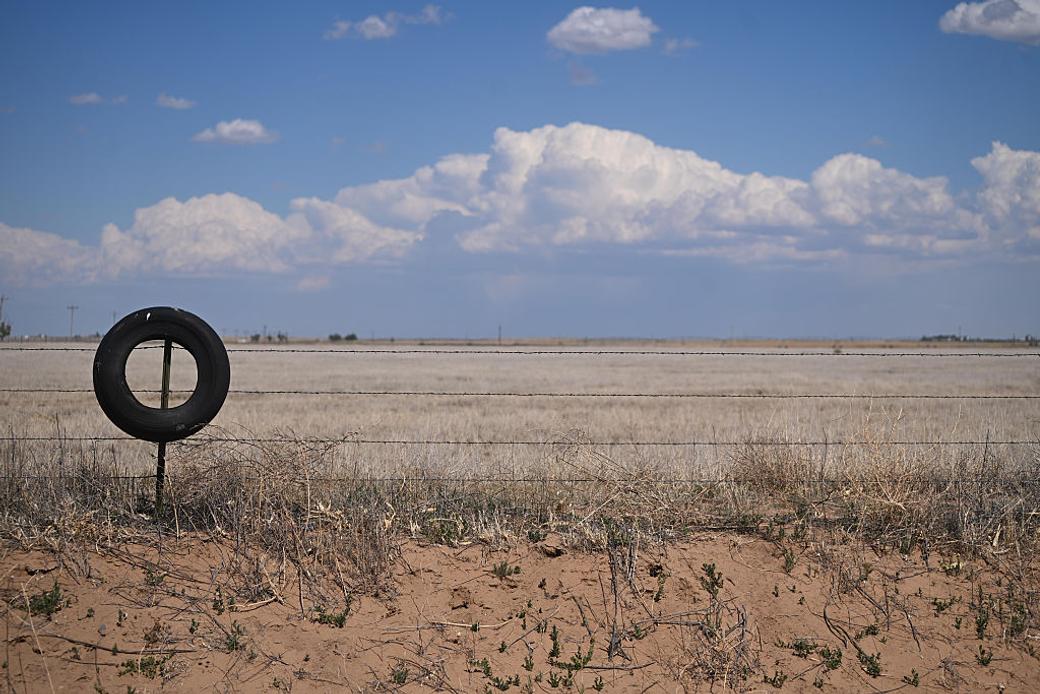 An old tire hangs on a barbwire fence overlooking a dry landscape.