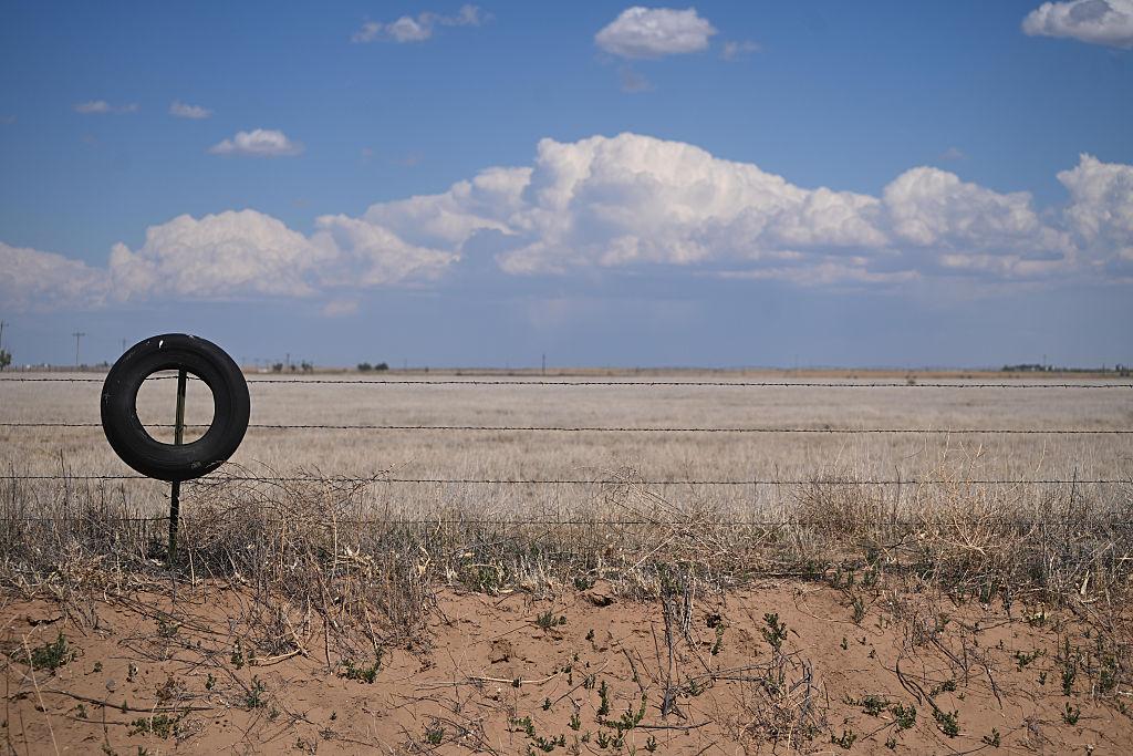An old tire hangs on a barbwire fence overlooking a dry landscape.