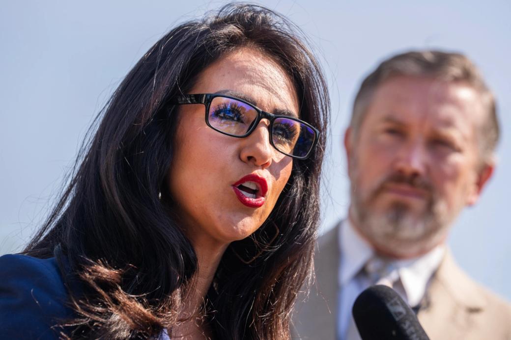 Person giving speech into a microphone with person in the background