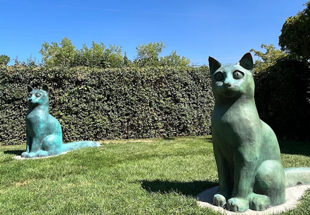 Two four-foot tall bronze cat statues in a park. 