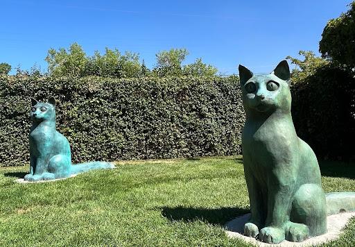 Two four-foot tall bronze cat statues in a park.