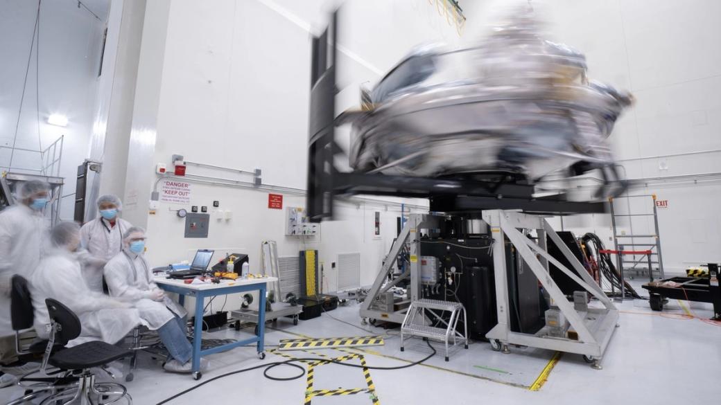 A silver, squat spacecraft spins at high speeds like a top while mounted on machinery.