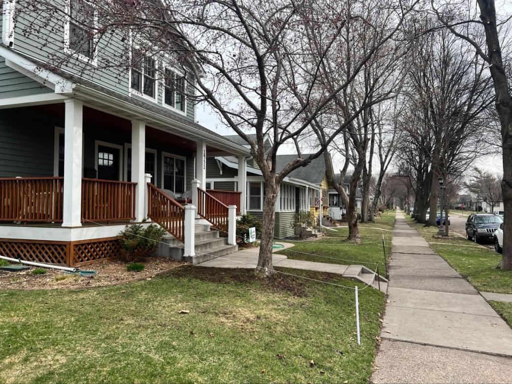 A view down a sidewalk with a few two-story homes on the left, with white pillars. Bare trees also line the sidewalk.