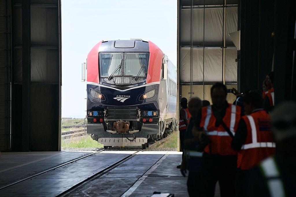 Workers in reflective vests watch an Amtrak train enter a passenger rail services building of the Transportation Technology Center in Pueblo, Colorado