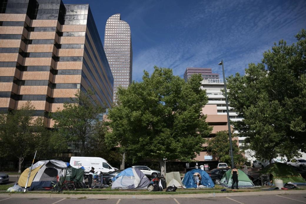 Several tents next to a parking lot, with trees and tall buildings in the background.