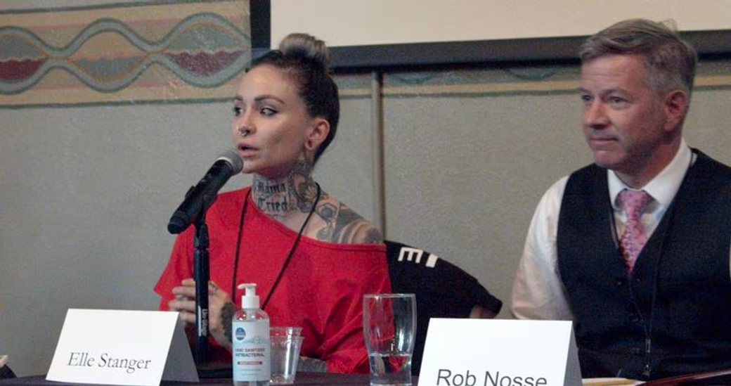 Person in red top and tattoos on neck (left) with person wearing black vest and pink tie(right), names in front of them.