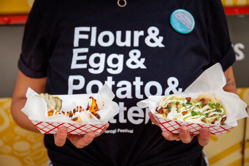 someone wearing a shirt that says Flour & Egg & Potato & Butter, holding two trays of pierogi