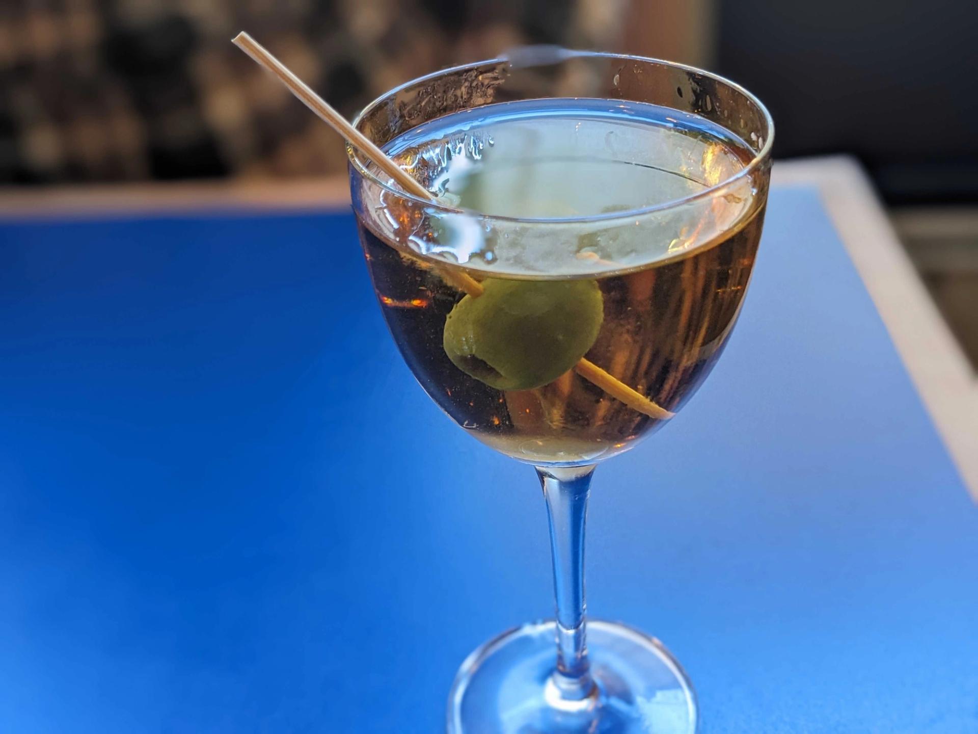 olive in a drink on a blue table.