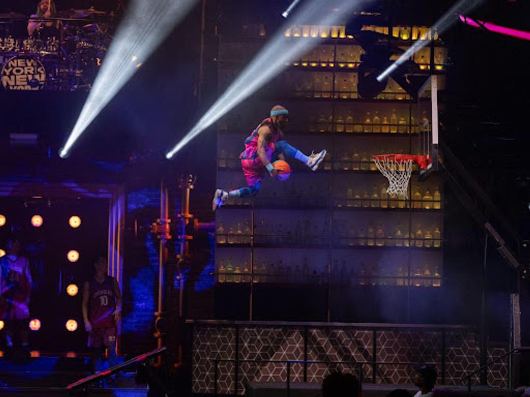 A Cirque du Soleil performer leaps toward a basketball hoop.