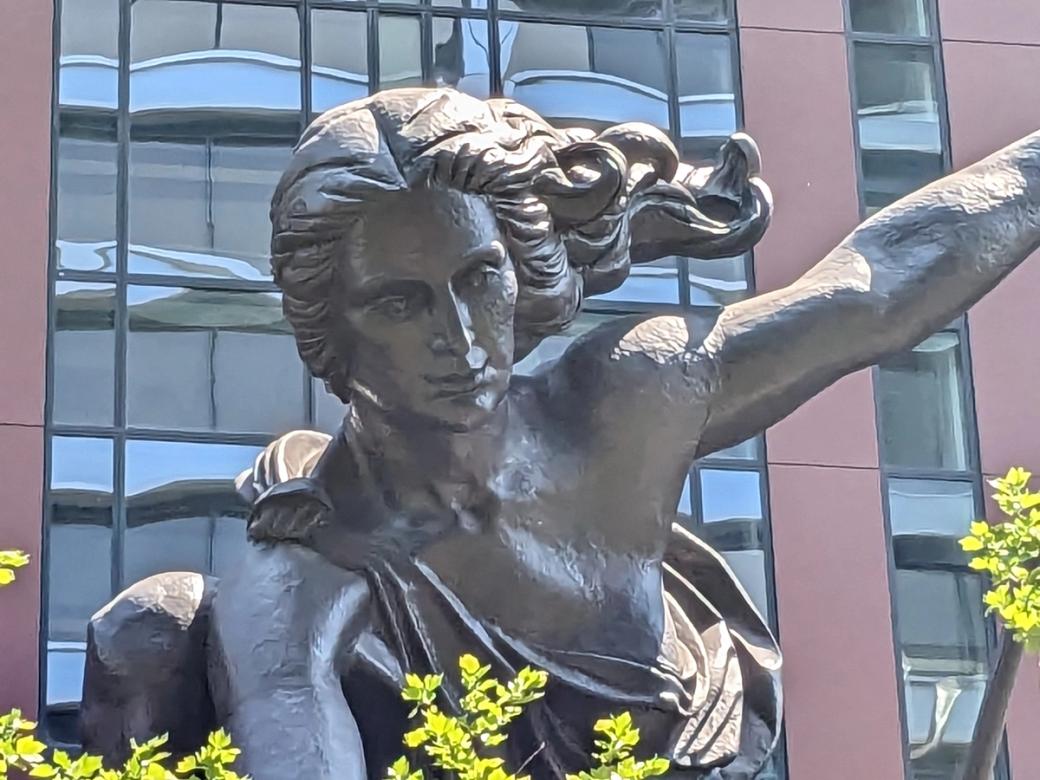 bronze toga-clad sculpture with red building in background 