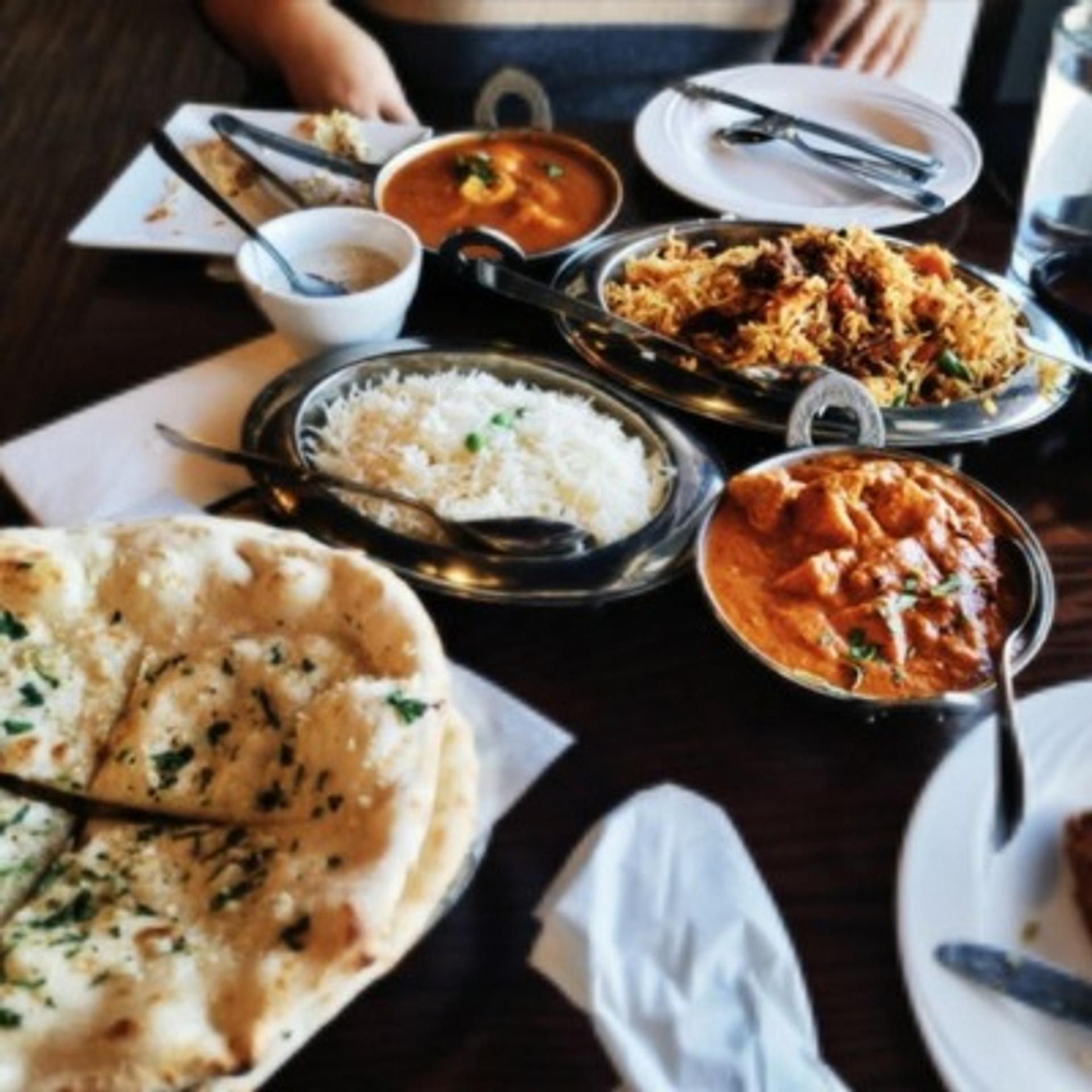 A table with an arrangement of naan, different kinds rice dishes, different curries and soup.