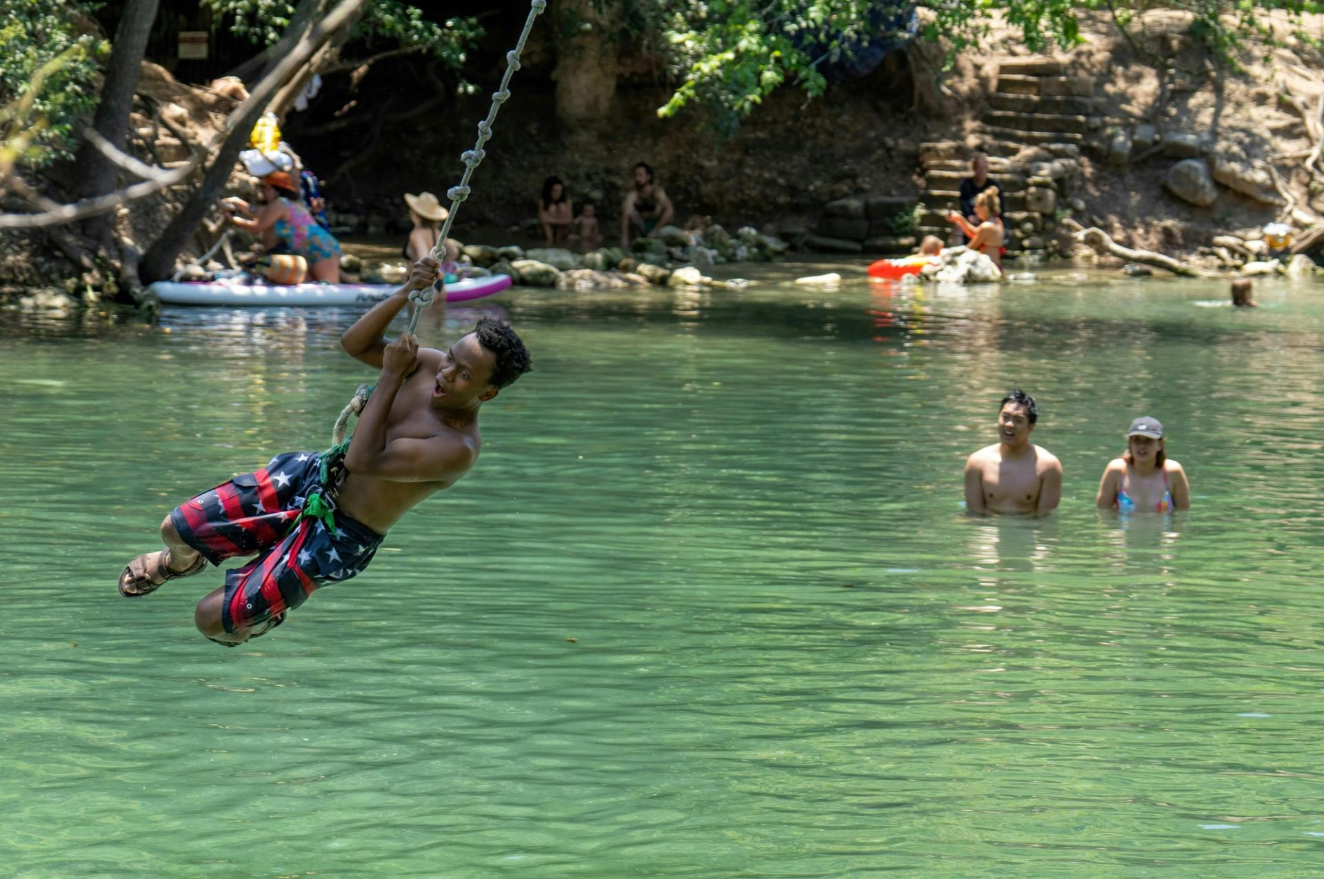 A child swinging on a rope into water.