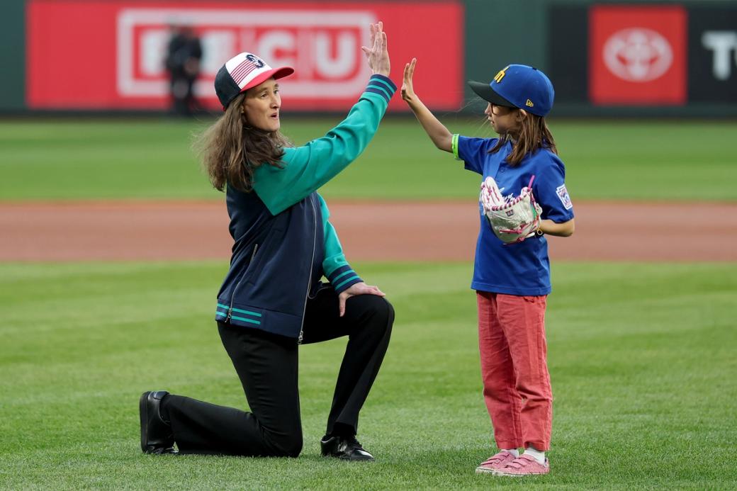 Seattle Mayor Katie Wilson high fives a young fan in a blue Mariners hat and jersey after the ceremonial first pitch.