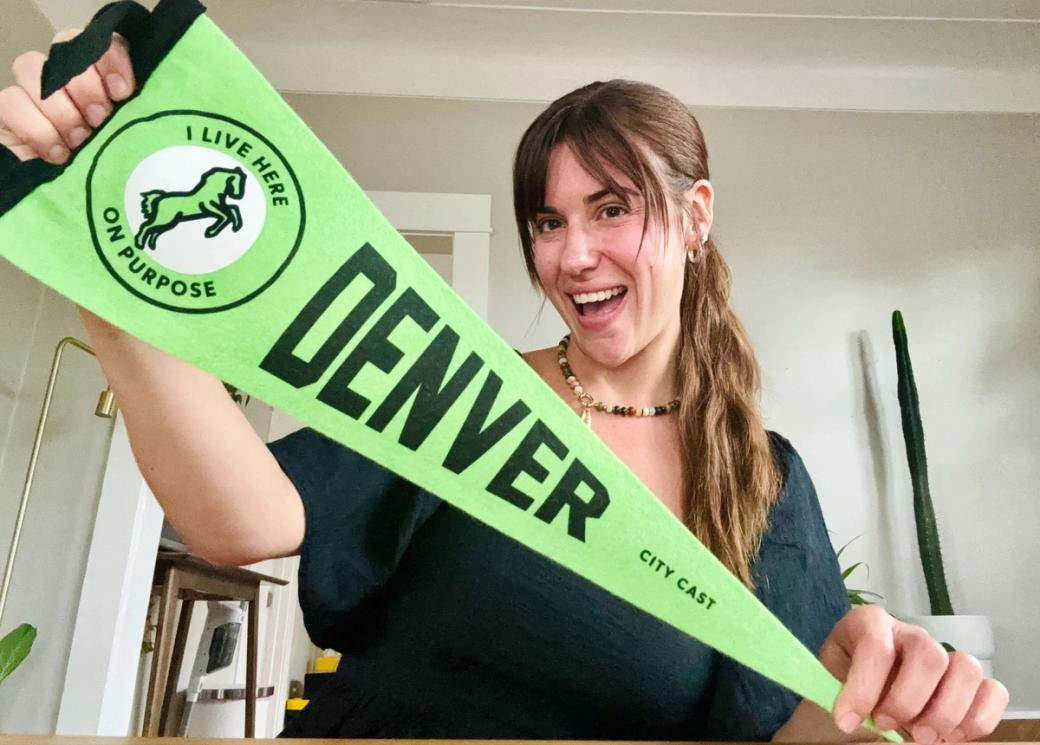 Michelle Polizzi holds up the cool City Cast Denver pennant.