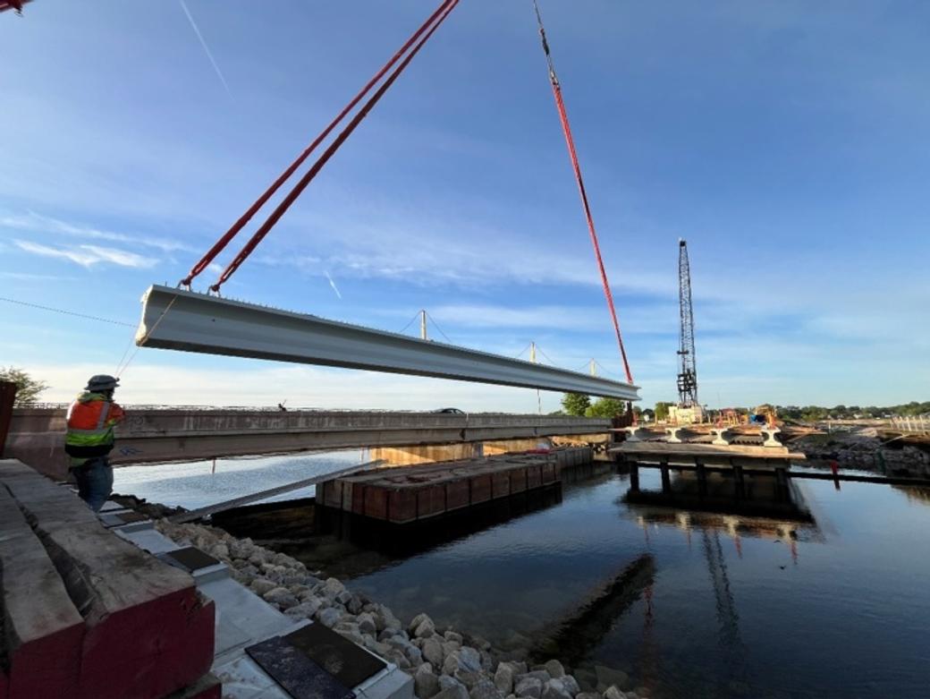 A crane lifts a giant concrete beam over water.