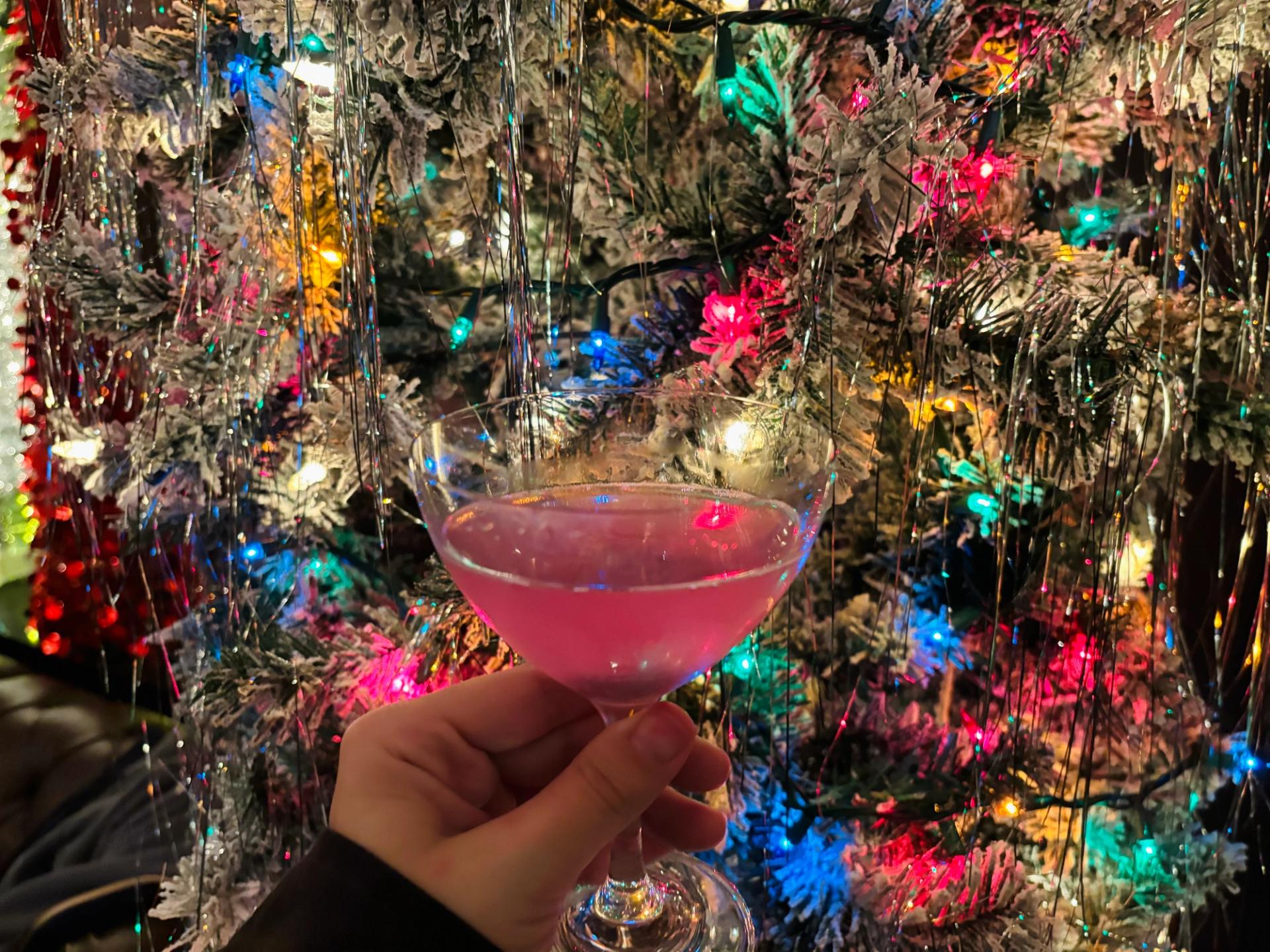 a pink cocktail in front of a colorful christmas tree