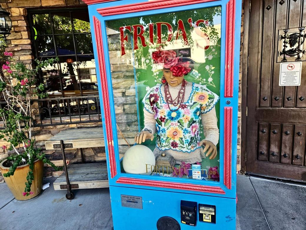 A turquoise fortune-telling machine with "FRIDA'S" written on the glass