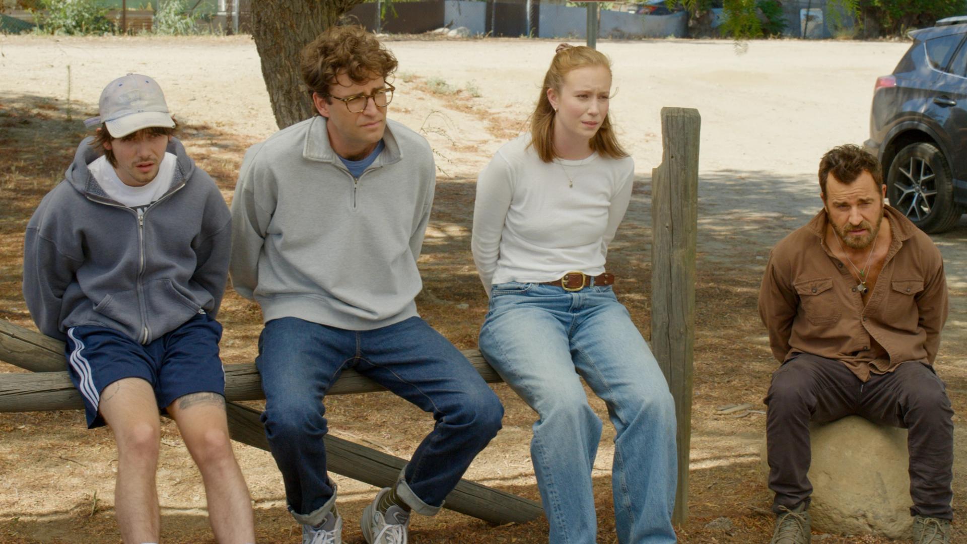 Griffin Gluck, John Reynolds, Hannah Einbinder, and Justin Theroux sitting on a fence with their hands in handcuffs.