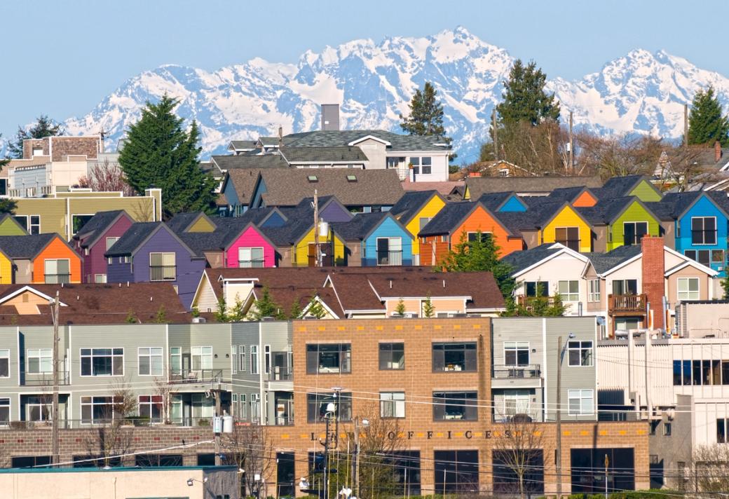 A row of colorful townhouses set in and around houses and apartment buildings with a snow covered Olympic Mountain range in the background