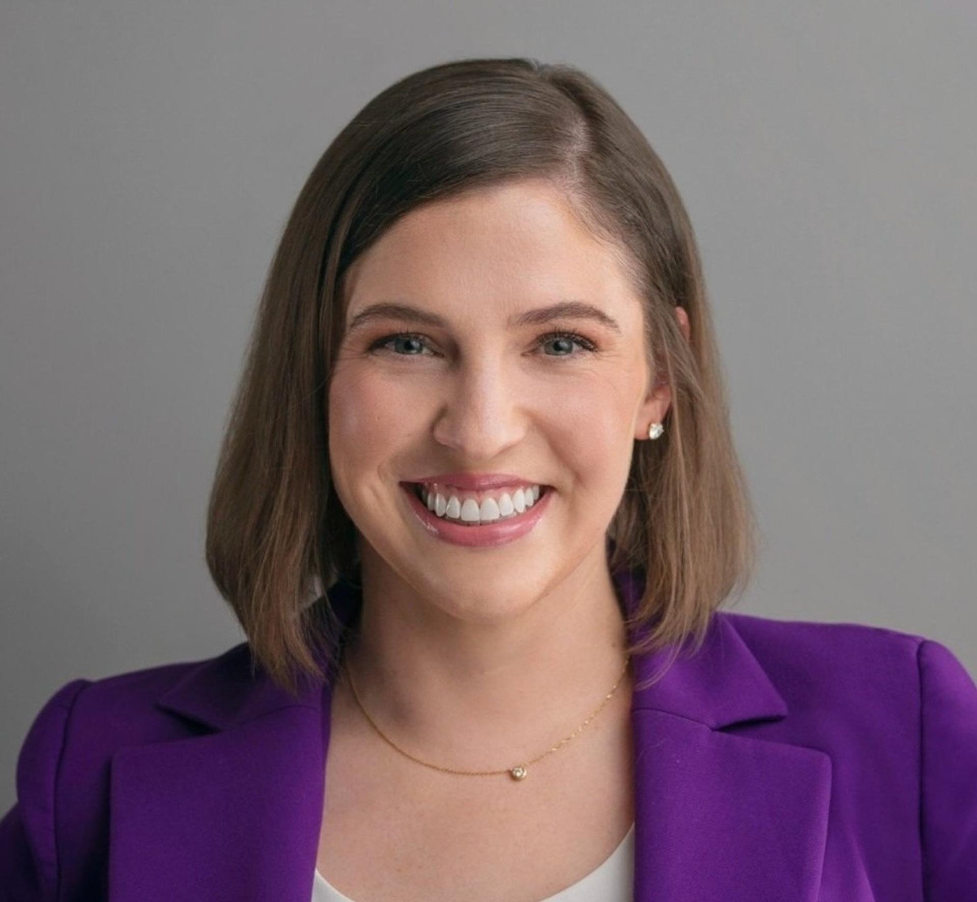 A photo of a woman smiling with a purple blazer on