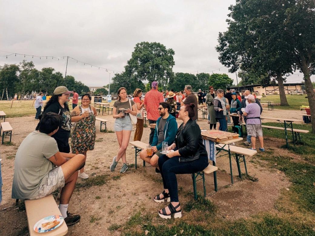 A group of people sit at picnic benches in a park.