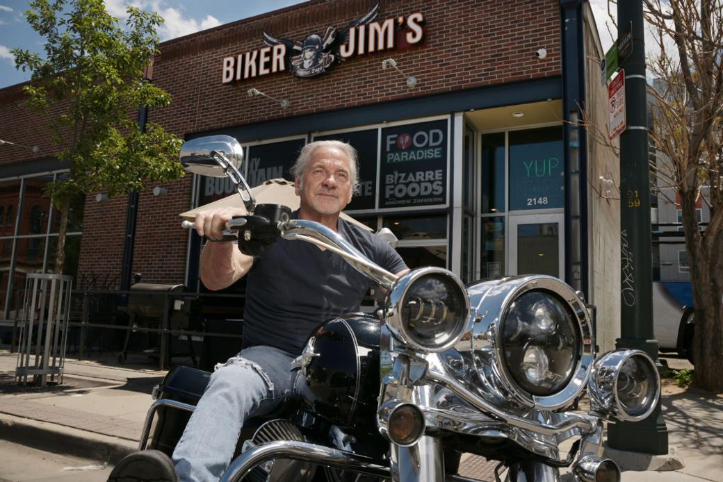 “Biker Jim” Pittenger poses on his Harley outside the (now-closed) iconic Denver  business he used to own, Biker Jim’s Gourmet Hot Dogs.