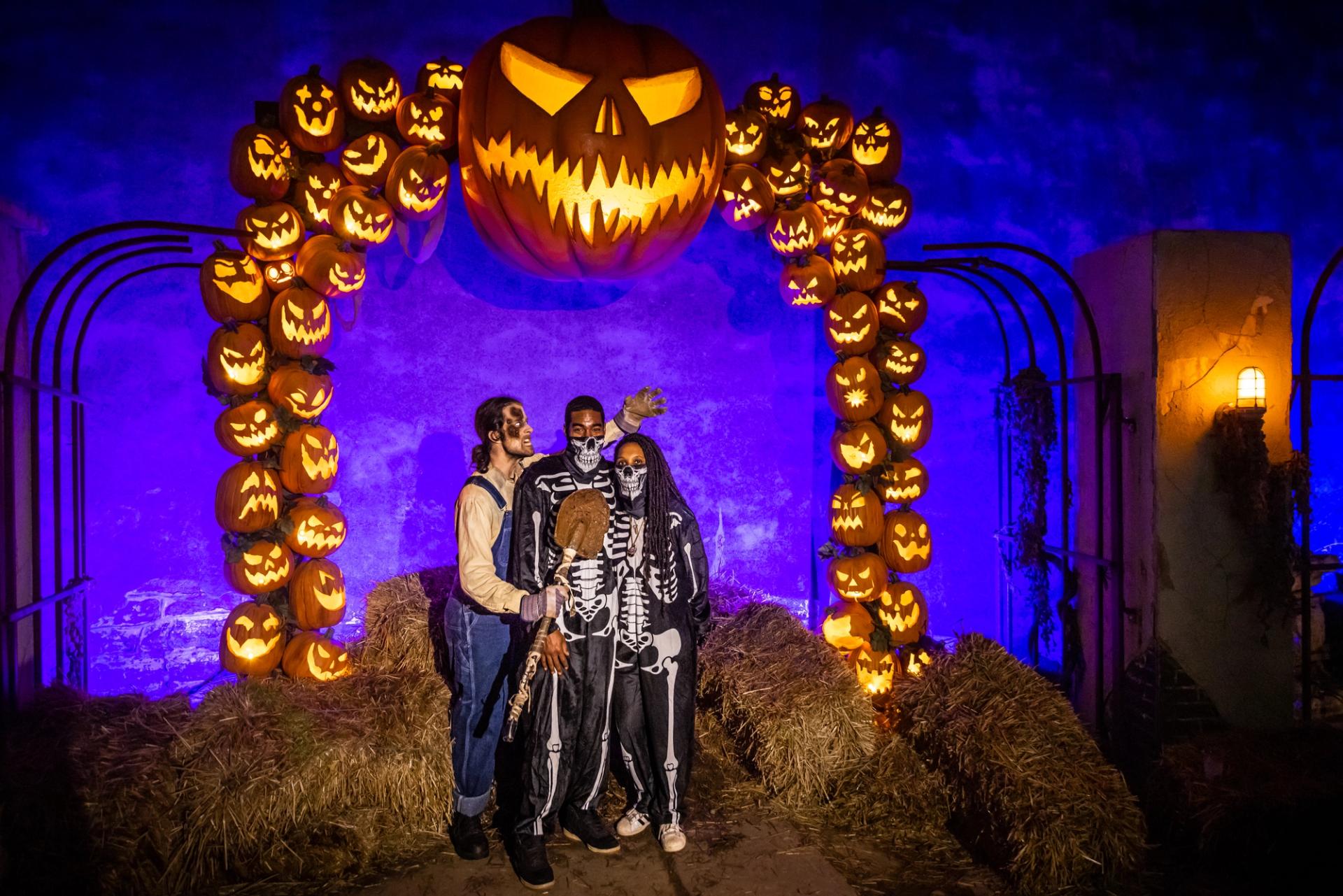 Three people wearing costumes under an arch made of creepy jack-o-lanterns.