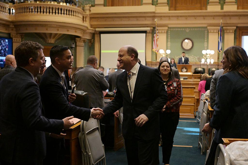 Gov. Jared Polis in a black suit shaking hands with a man in the colorado assembly