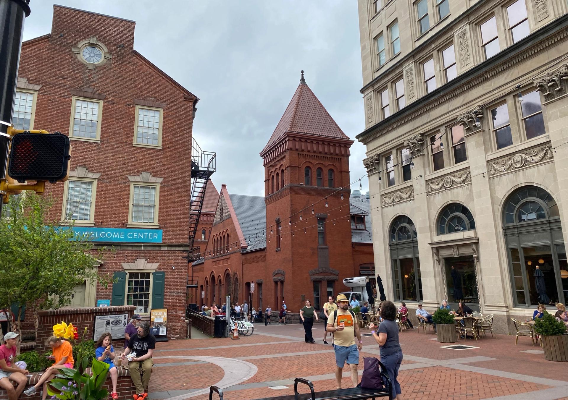 A scene from downtown Lancaster, including people sitting in and walking through the plaza near Lancaster Central Market.