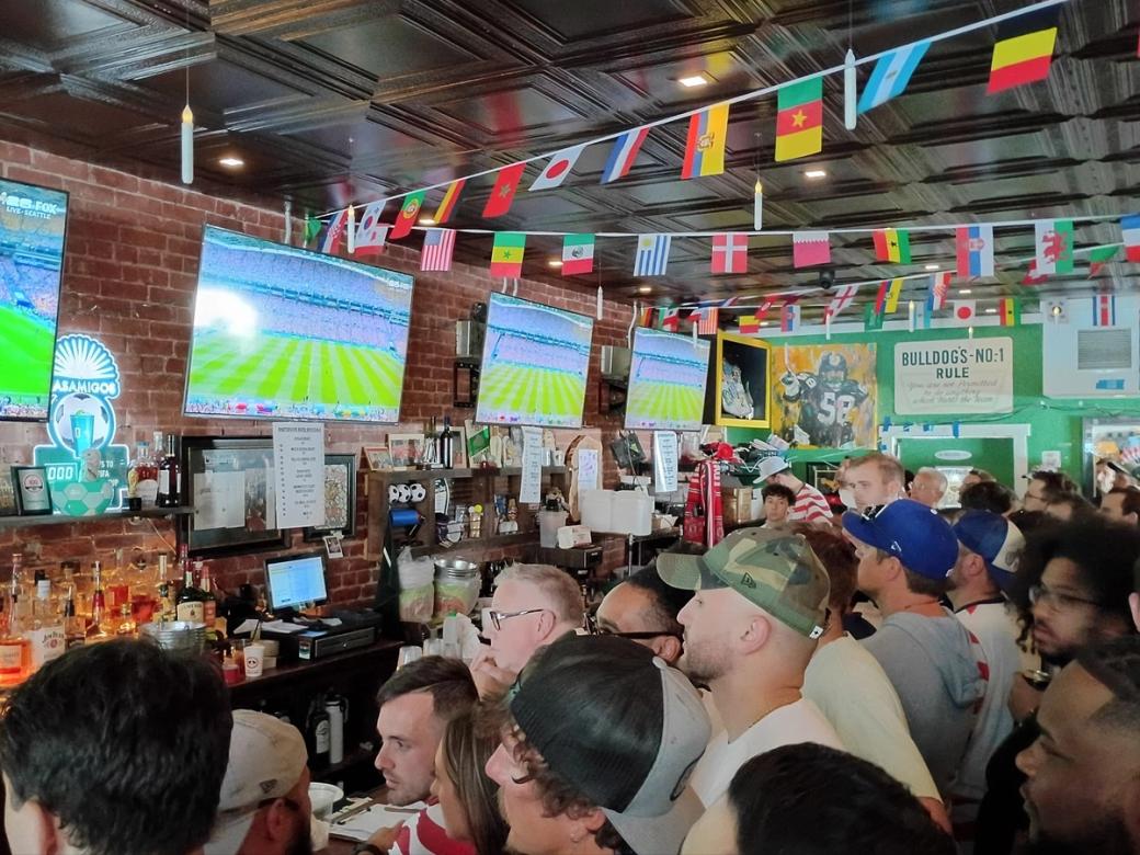A crowd at a bar watches soccer on several televisions.