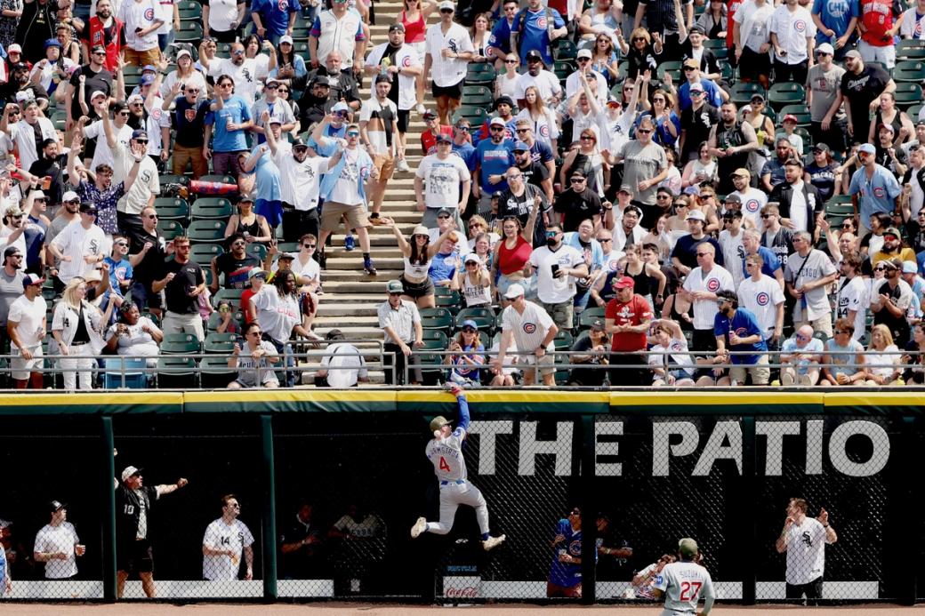 Pete Crow-Armstrong #4 of the Chicago Cubs misses a fly ball double at the wall, while many Cubs and White Sox fans look on in the background.