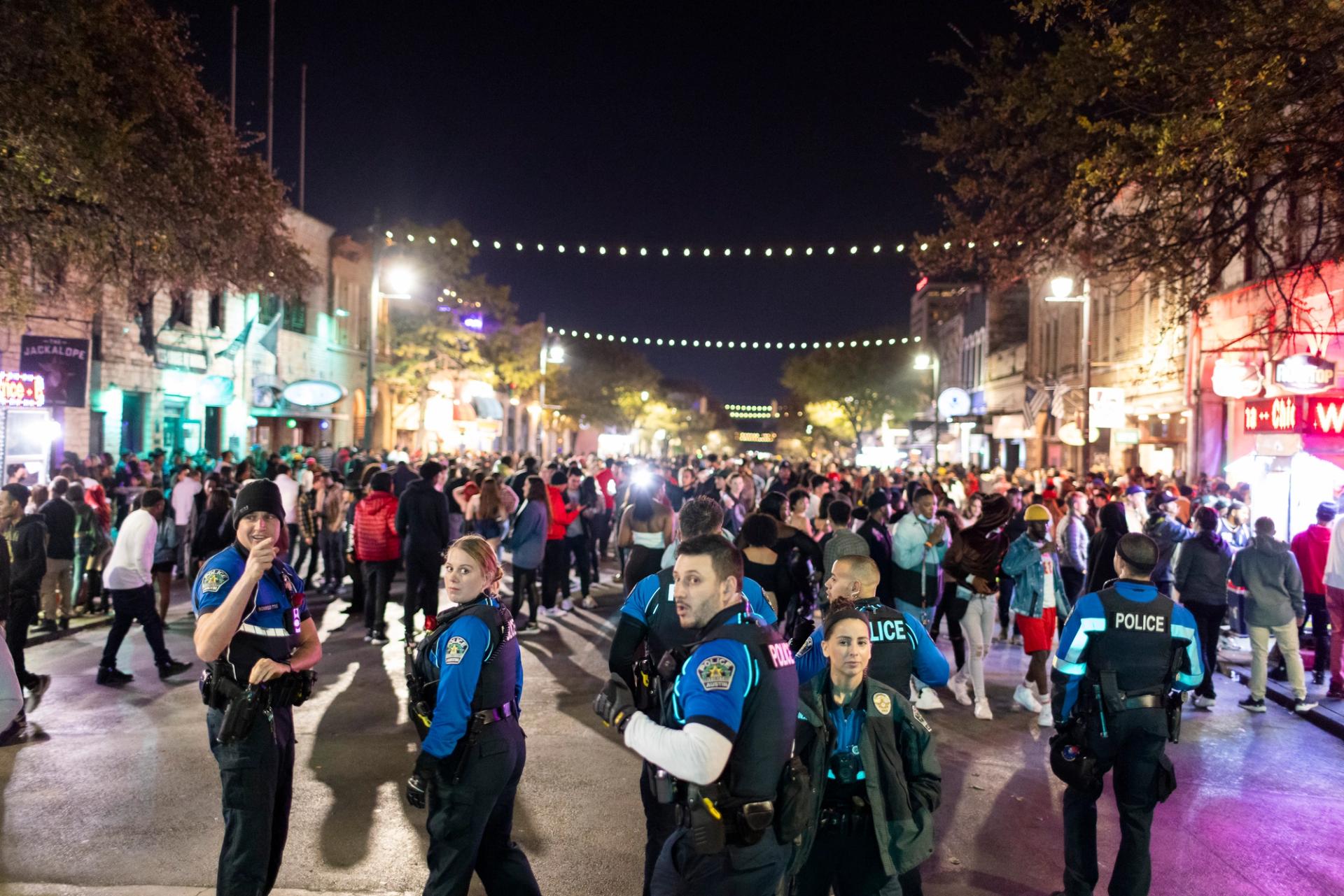 A street crowded with people at nighttime. Austin police officers are lining the street in blue and black uniforms.