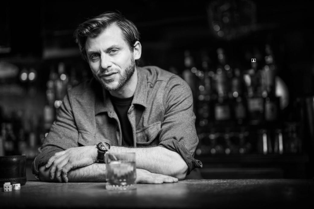 A man sitting at a bar with a glass of whiskey in front of him.