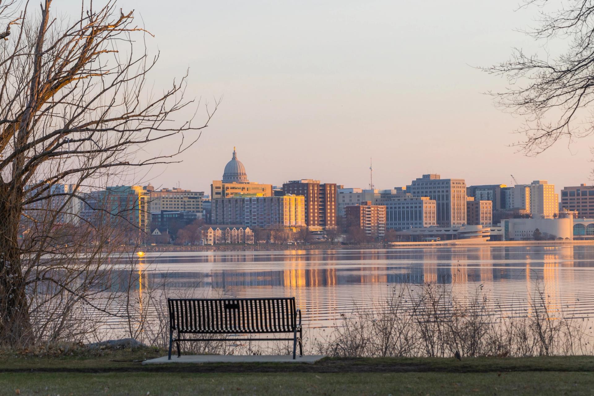 A park bench over looking a lake and Madison's skyline.
